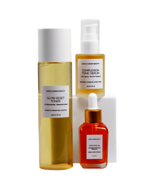 A layered product display of Marula Green Beauty skincare featuring Complexion Tonic Serum stacked high on a central white pedestal with Fade Face Oil and Glow Reset Toner placed around it.